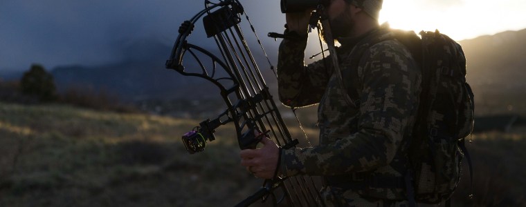 Photograph of hunter with bow looking through binoculars