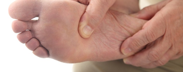 Photograph of elderly man checking his aching foot, close up