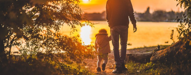 Photograph of daughter and father walking toward a lake at sunset