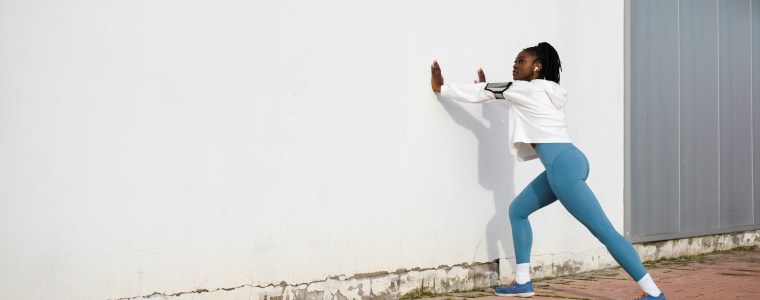 Photograph of female athlete training outside; stretching her calf muscles before a run.